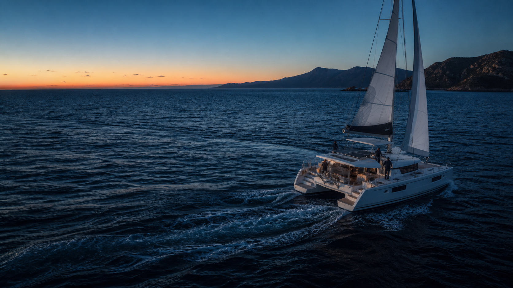 A sailing catamaran following its course along the coast at blue hour