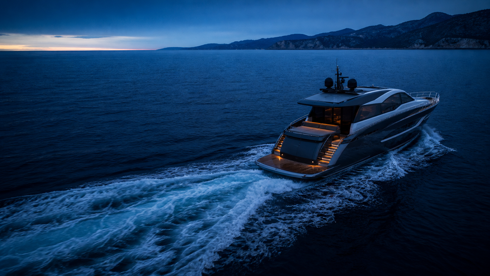 A 60-foot motor yacht moving along a rugged coastline at blue hour