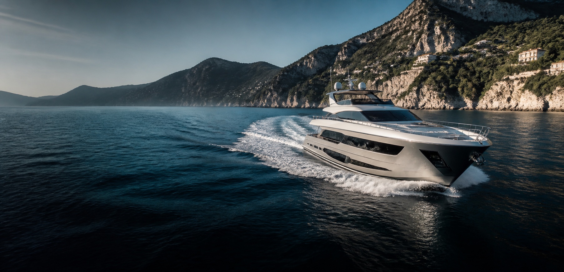 Modern motor yacht cruising through deep blue water beside a Mediterranean coastline
