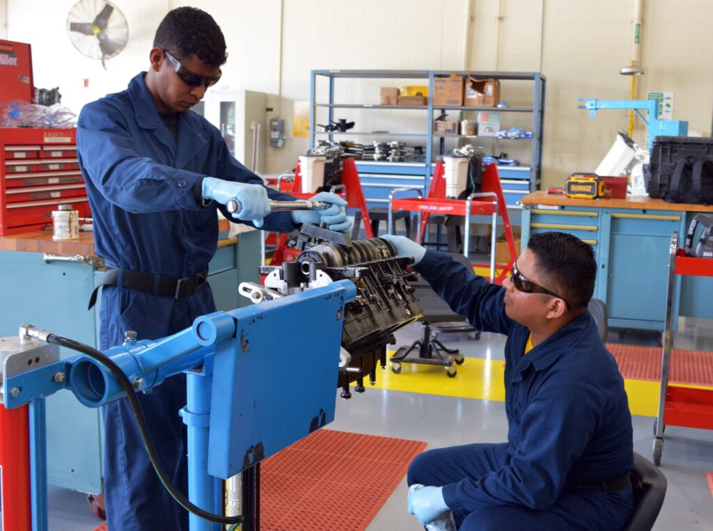 Marine mechanics working on a disassembled outboard powerhead in a real workshop